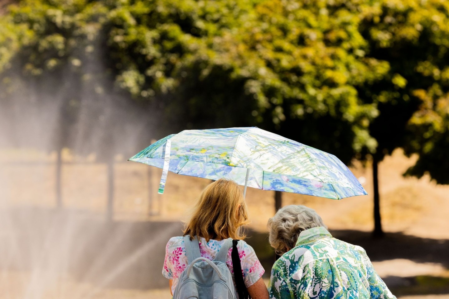 Zwei Frauen schützen mit einem Regenschirm vor der Sonne.